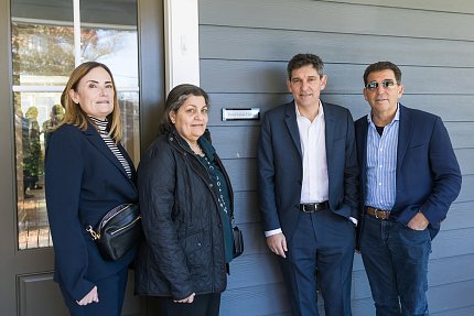 Two women and two men stand outside doorway of house, with plaque showing name Phil Leder House