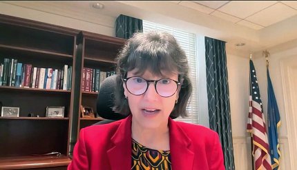 Screenshot of Bertagnolli speaking into computer screen with office shelves behind her