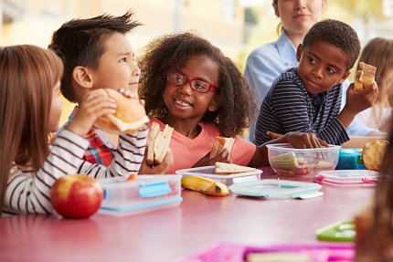 A group of children eat lunch outdoors.