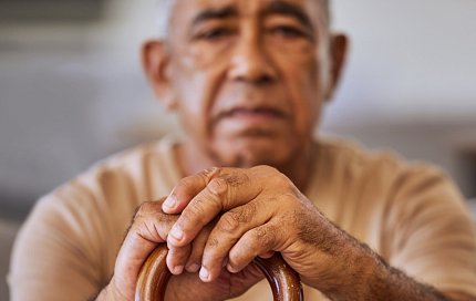An older man with serious face rests his hands on a cane.