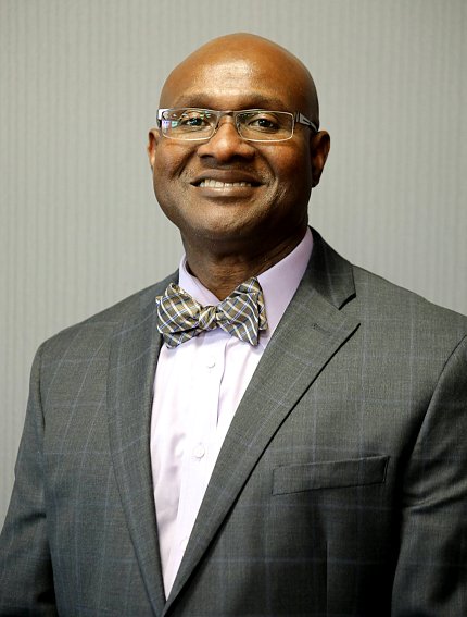 Black man wearing suit and bowtie, glasses, smiling 
