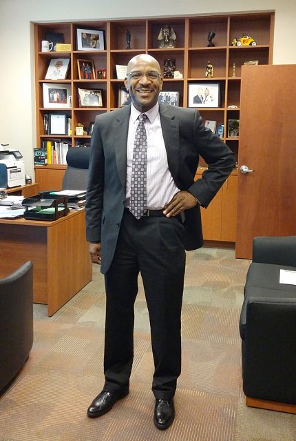 Spruill stands in an office, smiling, with his left hand on his hip.