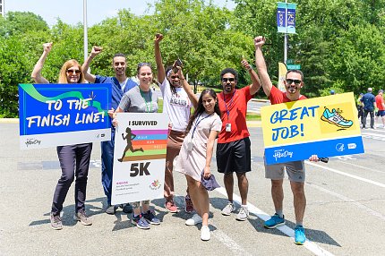 A group cheers together in a parking lot, holding motivational posters.