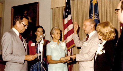 Man holds right hand up with left hand on book as woman holds book and another man reads from handheld card. Looking on are two additional women and a thrid man.