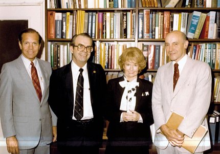 Three men and one woman stand in front of a bookcase.