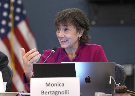 Dr. Bertagnolli seated, talking, hand cupped, with laptop on table