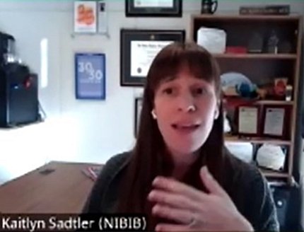 Dr. Kaitlyn Sadtler, hand to chest, talking on screen from home office