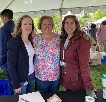 Three women pose outside on NIH's main campus under a tent