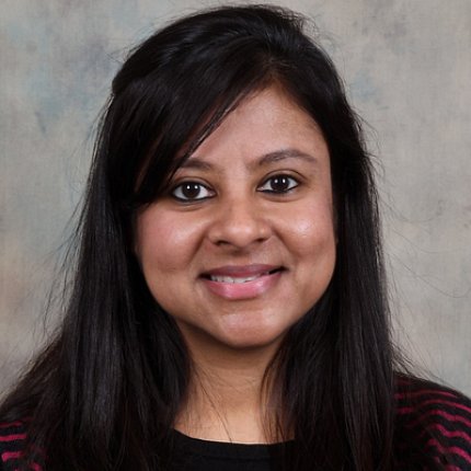 Headshot of Sen, who is smiling and positioned in front of a gray background.