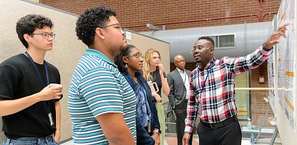 A student points to his poster as other students look on.