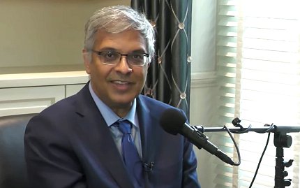 Dr. Bhattacharya smiling, seated by microphone