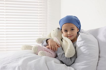A young cancer patient wearing a blue cap cuddles a toy bunny .