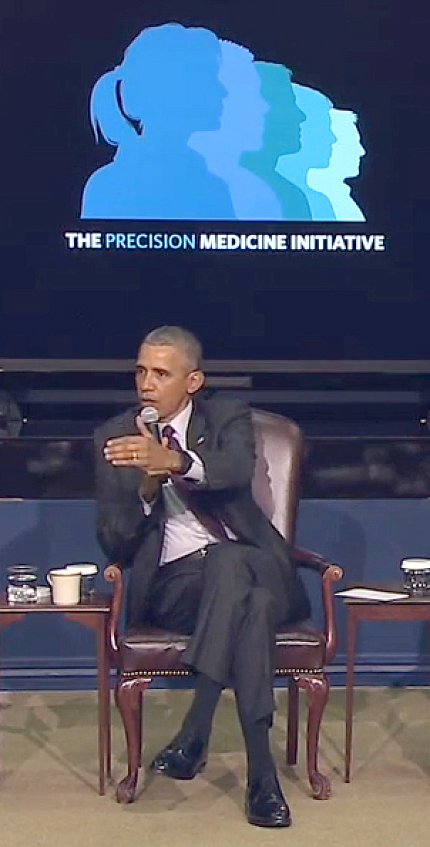 President Barack Obama partiWith mic in one hand, Obama gestures with other hand while seated in front of a projected slide.cipates in PMI summit panel Feb. 25 at the White House. 
