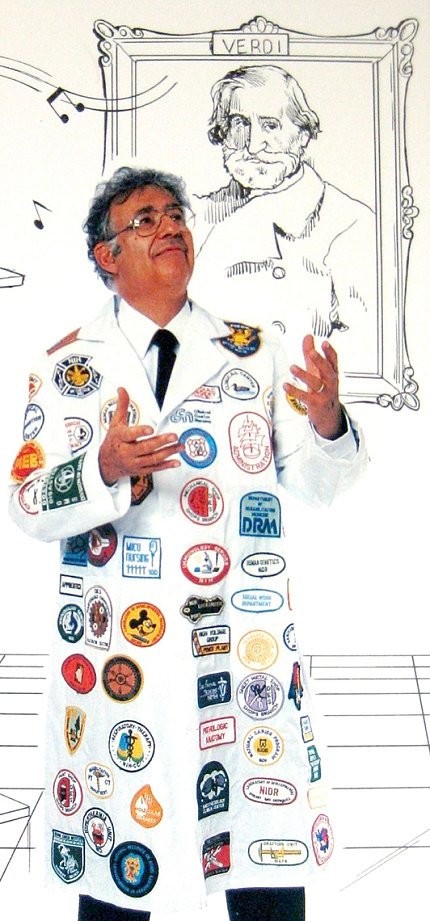 Rosen wears a lab coat with logos while standing in front of a cartoon portrait of Verdi