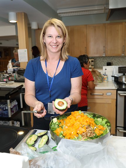 Gardner smiling, slicing avocado behind big bowl of salad
