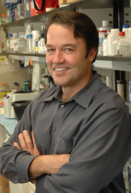 A smiling Dr. Tisdale stands, arms folded, in his lab.