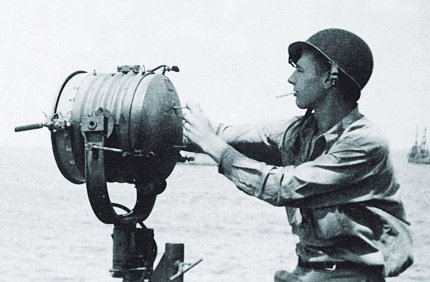 In uniform with helmet, Gardner operates a giant spotlight during WWII. 