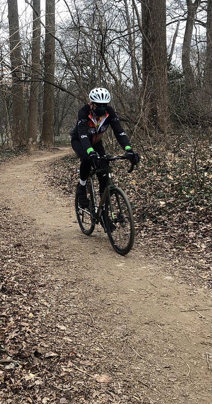 Kern in mask and helmet, riding bicycle on path through wooded area