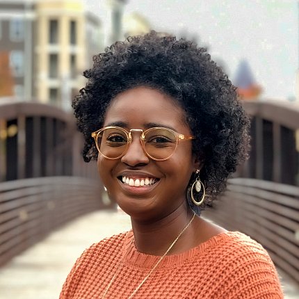A smiling Velencia Witherspoon in an orange sweater standing on a bridge