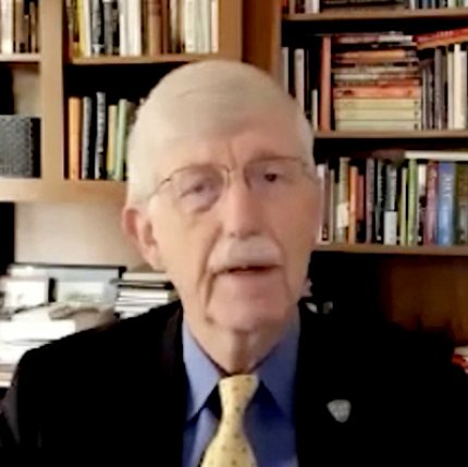 Screenshot of Collins, seated, wearing dark jacket, blue shirt and yellow tie, with bookcase behind him
