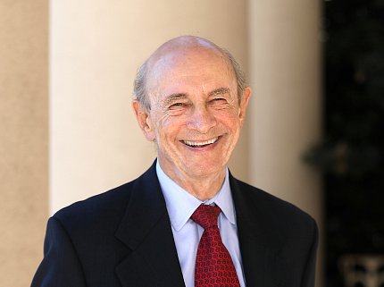 A smiling Harvey Alter stands in suit, red tie outside.