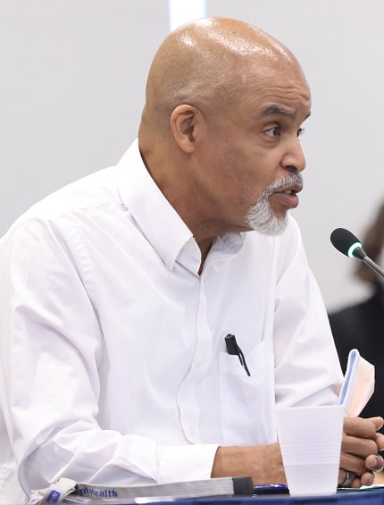 Burton, seated at table, speaks into mic.