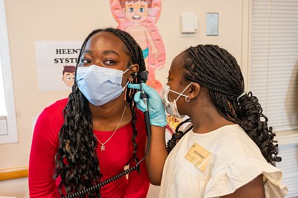 Child uses an otoscope to look into her sister's ear.