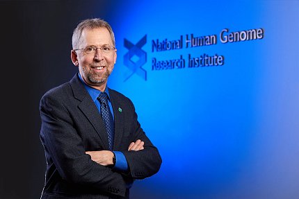 Green stands with arms crossed in front of blue wall with institute name beside double helix graphic