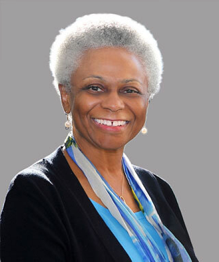 Dr. Bernard stands against a gray background. She is smiling and wearing a black jacket, blue shirt and blue lanyard.