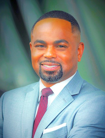 headshot of Black man in blue suit, white shirt, red tie