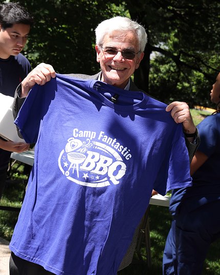 A smiling man shows off a purple Camp Fantastic BBQ t-shirt.