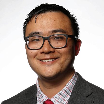 Lee, wearing glasses and a suit, smiles against a white background.
