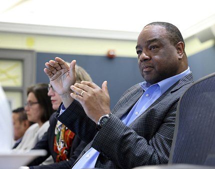 A man gestures with his hands as he speaks from his seat at the conference table.