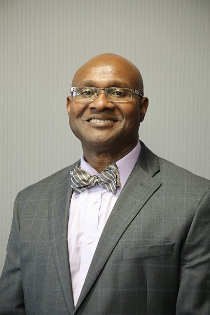 Headshot of Egede, wearing glasses, a suit and a striped bow tie.
