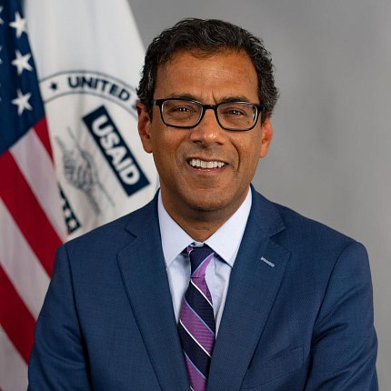 Gawande sits for a portrait with the American and USAID flags behind him.