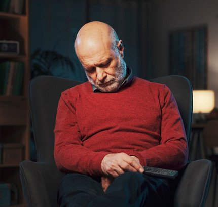A man sleeps in a chair with his chin resting on his chest.
