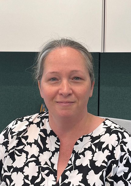 A smiling Keegan, wearing a patterned black-and-white shirt, seated in an office.