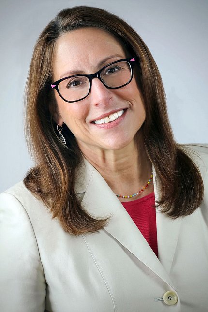 Donenberg, wearing glasses and a white suit jacket, smiles against a white backdrop.