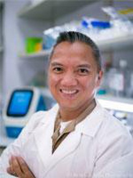 Photo of Saligan standing in front of white shelving stocked with lab materials