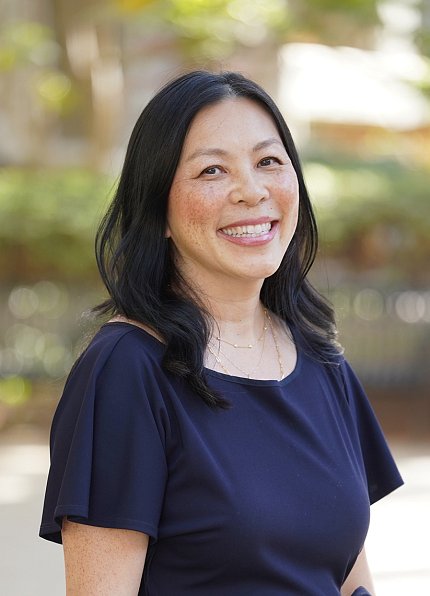 Lau smiles over her right shoulder at the camera. The background is blurred but appears to be an outdoor garden.
