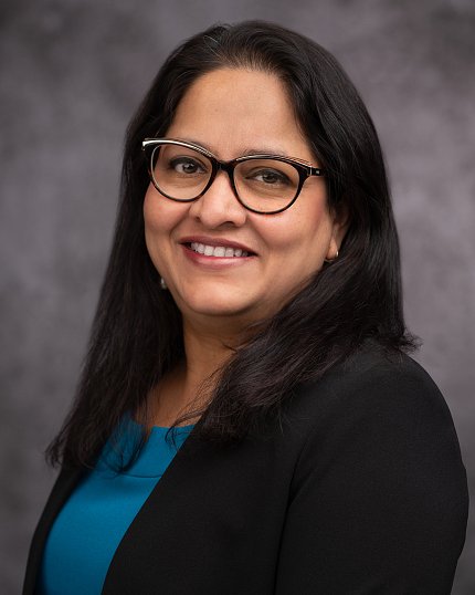 Headshot of Chakrapani, who is smiling over her shoulder against a gray background.