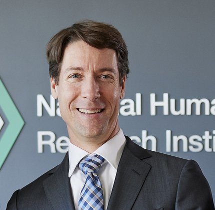 Phillippy stands in front of a gray-blue wall bearing an NIH logo.