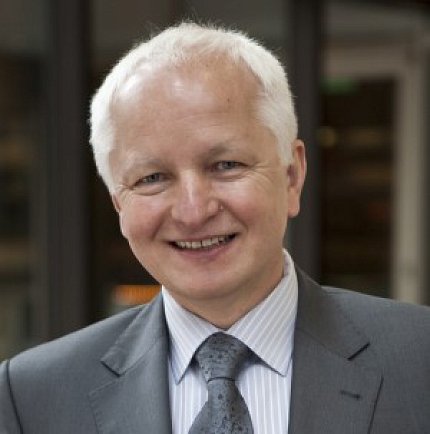 Rewers, wearing a suit and tie, smiles at the camera.