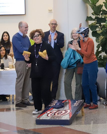 Zenk, smiling, holds beanbags in each hand, surrounded by cheering colleagues.