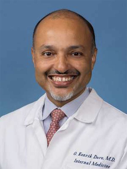 Duru, smiling, in white lab coat and tie