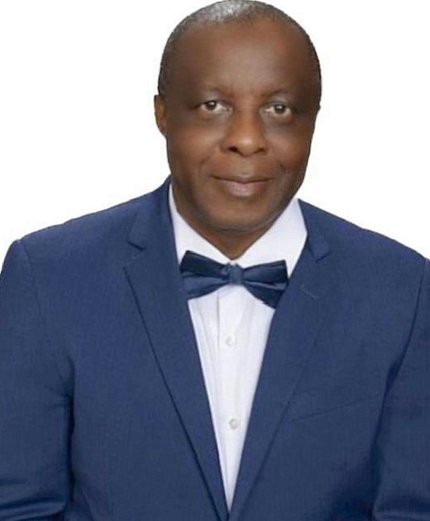 Musa, wearing a navy suit and bow tie, smiles at the camera.