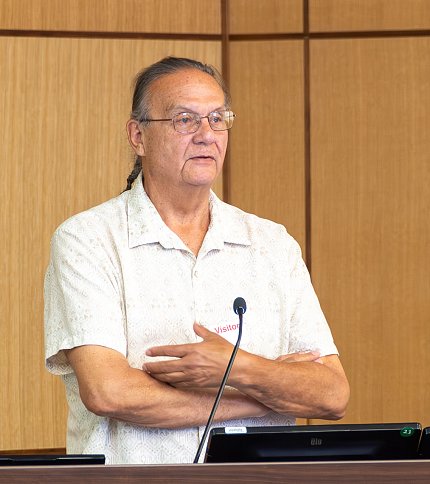 Doyle, with arms folded, speaks into mic.