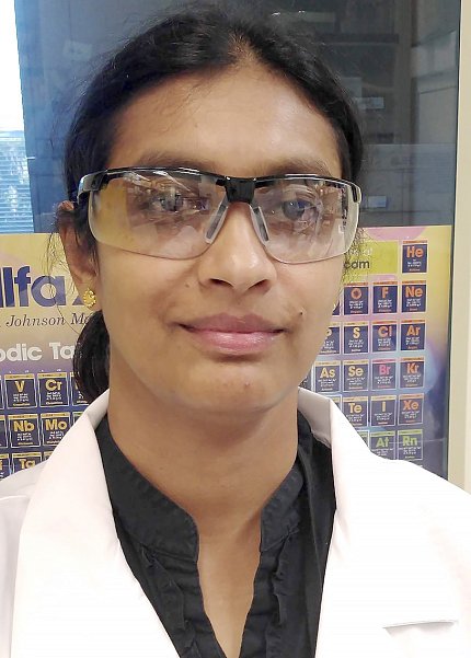 Iyer, wearing lab glasses and a white coat, smiles for a selfie against a window.