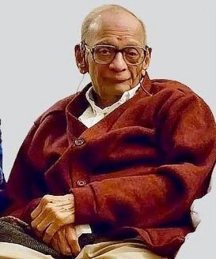 Ram, wearing glasses and a red jacket, smiles at the camera.