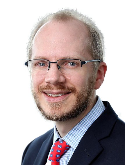 headshot of white man with mustache, beard, and glasses, wearing suit and tie